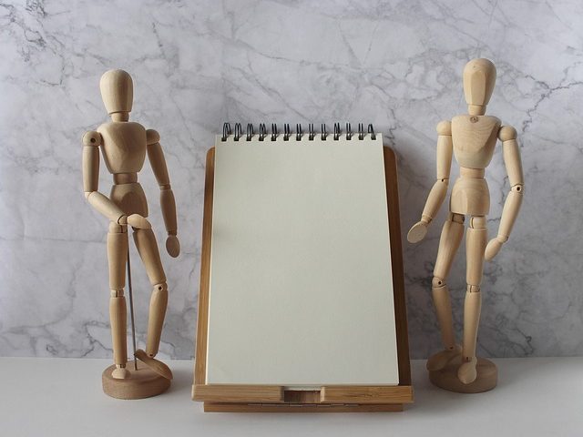 Zwei Holzfiguren stehen neben einem Schreibblock