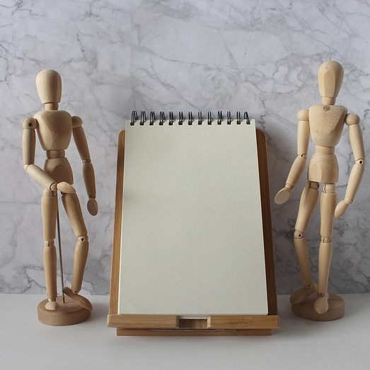Zwei Holzfiguren stehen neben einem Schreibblock
